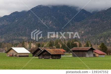 Small wooden houses in green field with mountain forest background Bavaria Germany 139147332