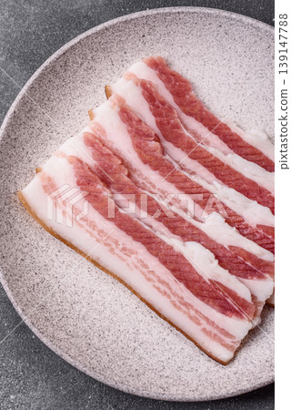 Raw fresh bacon slices with layers of meat or prosciutto prepared for frying. Raw bacon Raw fresh bacon slices with layers of meat or prosciutto prepared for frying. Raw bacon 139147788
