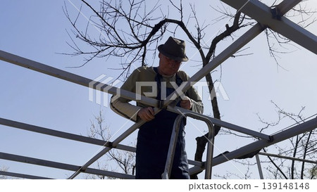 Male laborer uses a hammer to strike welded metal joints on carport frame. Adult worker refines and secures the structure, carefully adjusting welded connections metal installation work at the site 139148148