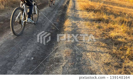 Young male friends ride mountain ski bikes along trail on sunny summer day. Beautiful golden sunlight at background. Concept of active lifestyle, adventure spirit and carefree weekend outdoor Young male friends ride mountain ski bikes along trail on sunny summer day. Beautiful golden sunlight at background. Concept of active lifestyle, adventure spirit and carefree weekend outdoor 139148164
