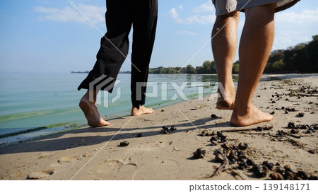 Bare feet of couple stepping together along sand beach at coastline. Male and female legs of pair walking near seaside. Happy lovers going along sandy shore. Concept of summer vacation or holiday Bare feet of couple stepping together along sand beach at coastline. Male and female legs of pair walking near seaside. Happy lovers going along sandy shore. Concept of summer vacation or holiday 139148171
