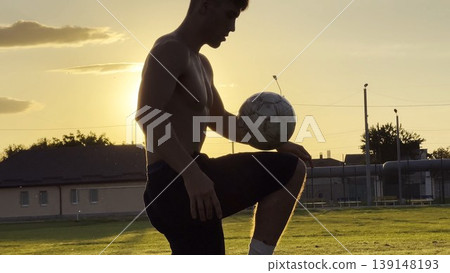 Young man juggling soccer ball on stadium at sunset. Professional footballer kicking ball at green field. Sportsman practicing tricks at meadow with sunlight at background. Freestyle football 139148193