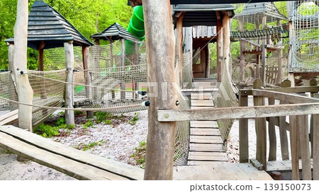 A wooden playground with a green slide and rope bridge for kids A wooden playground with a green slide and rope bridge for kids 139150073