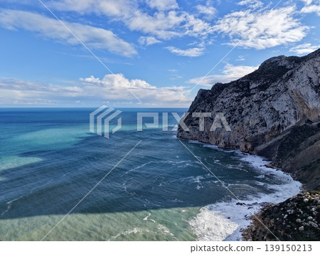 Vivid sea scene, Spectacular aerial view of vibrant surf hitting rugged stone structures under blue sky Vivid sea scene, Spectacular aerial view of vibrant surf hitting rugged stone structures under blue sky 139150213