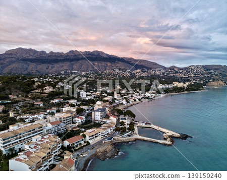 Serene seaside town at sunset, Peaceful shoreline settlement with colorful houses and mountain backdrop 139150240