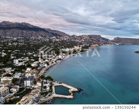 Calm sea meets peaceful mountain town, Dawn reflection captures quiet seaside village scene 139150244