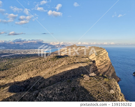 Mountain vista serenity, Cliffside view with peaceful waters, Sunset over rugged coast with shadowed rocks Mountain vista serenity, Cliffside view with peaceful waters, Sunset over rugged coast with shadowed rocks 139150282