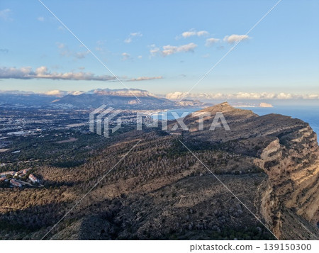 Steep ridges descend into shimmering blue waters, Rustic paths wind across rugged terrain by sea 139150300