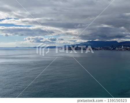 Peaceful ocean scene beneath moody clouds, Calm sea reflecting over mountains and gentle water surface Peaceful ocean scene beneath moody clouds, Calm sea reflecting over mountains and gentle water surface 139150323