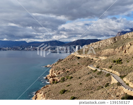 Trail along cliffs with ocean view, Walking path along rugged coast with distant cityscape view 139150327