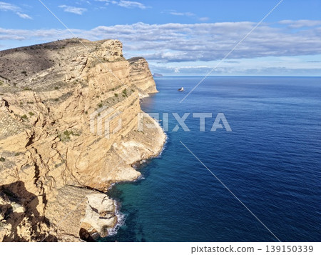 Isolated rocky cove with small harbor beneath towering cliffs and pristine turquoise waters Isolated rocky cove with small harbor beneath towering cliffs and pristine turquoise waters 139150339