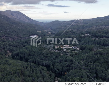 Secluded mountain village amid towering pines with winding roads and terraced fields at dusk Secluded mountain village amid towering pines with winding roads and terraced fields at dusk 139150406