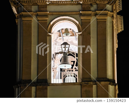 Quiet nighttime scene featuring ornate bell tower with aged bronze bell and textured stone details 139150423