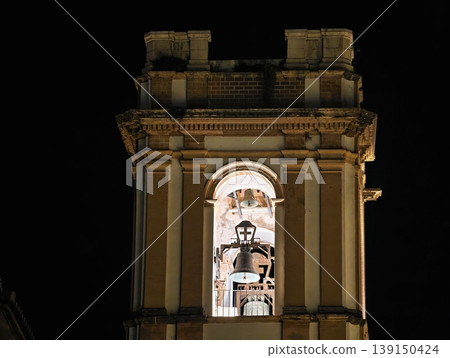 Bright bell tower. Grand brightly lit bell tower overlooking vibrant urban skyline during nighttime 139150424