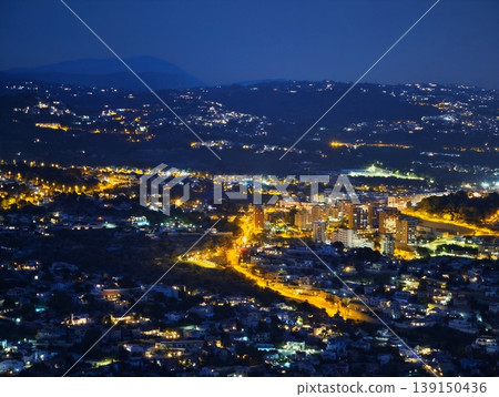 Night highway panorama. Night aerial view showcasing glowing highway alongside coastal hills and sea Night highway panorama. Night aerial view showcasing glowing highway alongside coastal hills and sea 139150436