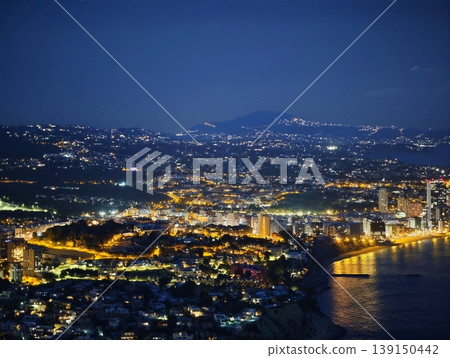 Silent seaside town with lights. Serene coastal harbor illuminated by city lights and mountain silhouette Silent seaside town with lights. Serene coastal harbor illuminated by city lights and mountain silhouette 139150442