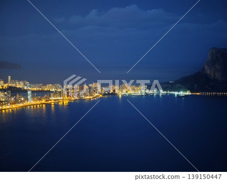 Vivid aerial view of illuminated coastline against dark ocean backdrop highlighting cityscape 139150447