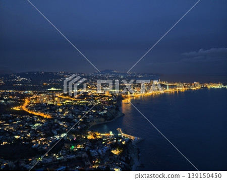 Vivid nightscape showcasing illuminated coastlines and deep blue sea under cloudy protection Vivid nightscape showcasing illuminated coastlines and deep blue sea under cloudy protection 139150450