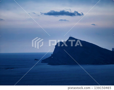 Calm maritime scene with gentle clouds. Silhouette of tranquil island against layered dusk sky atmosphere 139150465