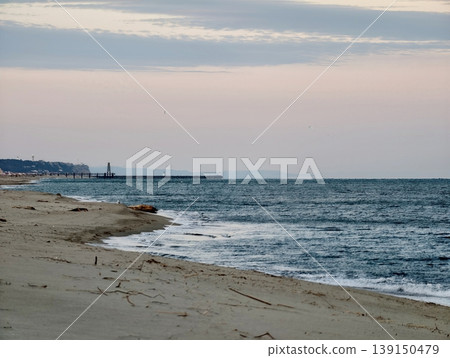 Serene shoreline with lighthouse silhouette. Calm coastal view featuring distant lighthouse and gentle waves Serene shoreline with lighthouse silhouette. Calm coastal view featuring distant lighthouse and gentle waves 139150479