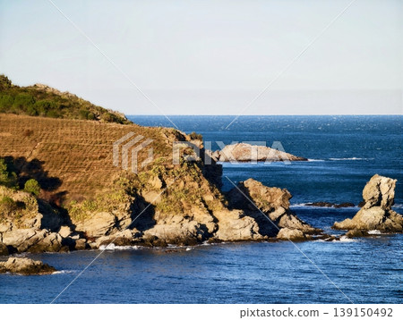 Bright cliffside view. Bright sun illuminates rocky promontory with deep blue ocean and expansive sky 139150492