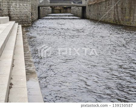 City waterway scene. Peaceful city canal with rippling water surrounded by concrete and stone structures 139150587