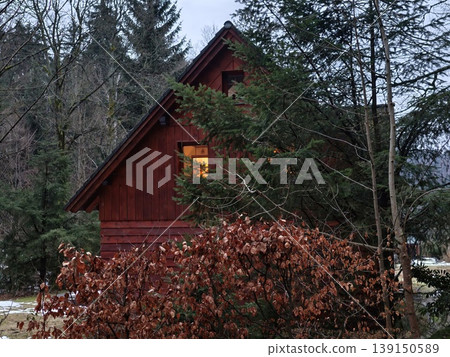Secluded forest hideaway with warmth. Serene woodland cabin glowing in dusky forest surroundings Secluded forest hideaway with warmth. Serene woodland cabin glowing in dusky forest surroundings 139150589