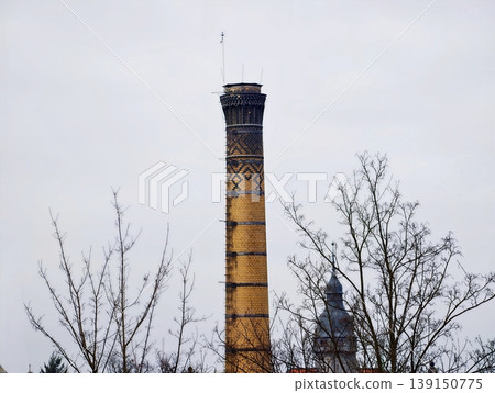Weathered brick with rising chimney. Old factory chimney above leafless trees with textured masonry 139150775