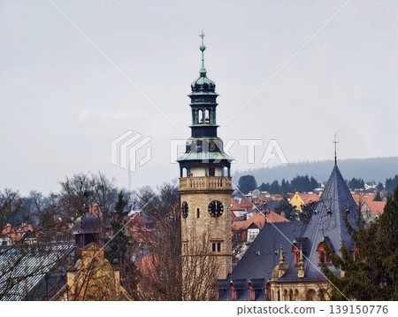Scenic old bell tower. An enchanting view of vintage bell tower amid lively roofs and green fields 139150776