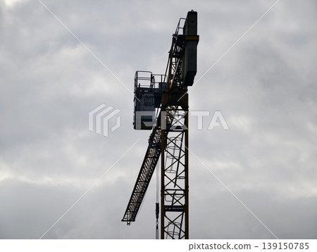 Industrial structure featuring crane silhouette beneath textured cloud cover with urban hints Industrial structure featuring crane silhouette beneath textured cloud cover with urban hints 139150785