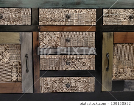 Decorative rustic storage unit featuring textured drawers and antique metal accents for warm interiors 139150832
