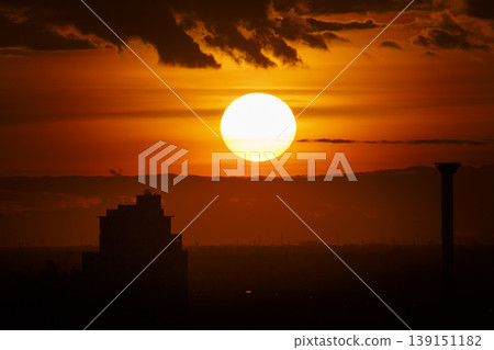 A large sun sets behind clouds in a dramatic red sunset sky 139151182