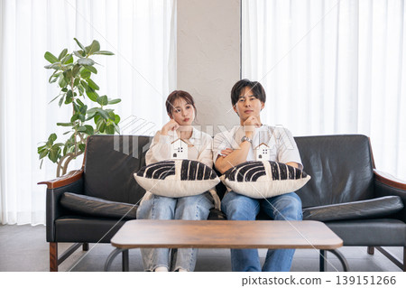 一對年輕夫婦坐在沙發上,看著他們親手製作的手工藝品,沉思著。 一對年輕夫婦坐在沙發上,看著他們親手製作的手工藝品,沉思著。 139151266