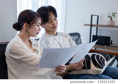 一對年輕夫婦坐在客廳沙發上,討論房屋設計方案。 一對年輕夫婦坐在客廳沙發上,討論房屋設計方案。 139151383