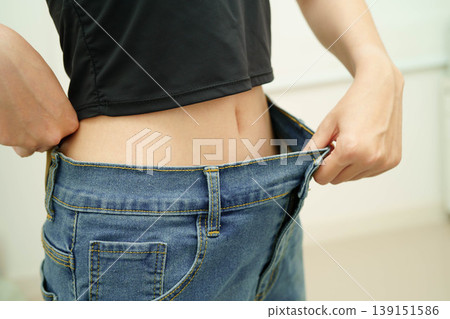 Young Asian woman losing weight wearing loose pants in oversize jeans. 139151586