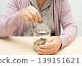 Retired elderly woman putting coins money in piggy bank and worry about monthly expenses and treatment fee payment. 139151621