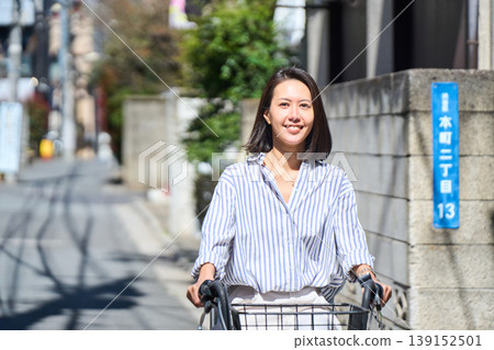 在陽光明媚的日子裡，一位日本女子微笑著騎著腳踏車。 139152501