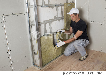 Worker in protective gloves insulating rock wool insulation in wooden frame for future house walls for cold barrier. Comfortable warm home, economy, construction and renovation concept Worker in protective gloves insulating rock wool insulation in wooden frame for future house walls for cold barrier. Comfortable warm home, economy, construction and renovation concept 139153026