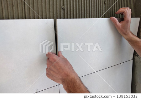 Worker hands putting ceramic tiles on the wall. Worker hands putting ceramic tiles on the wall. 139153032