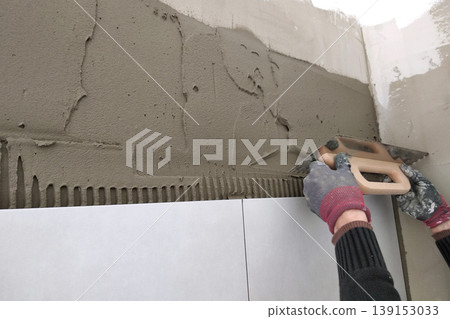 Worker hands putting ceramic tiles on the wall. Worker hands putting ceramic tiles on the wall. 139153033