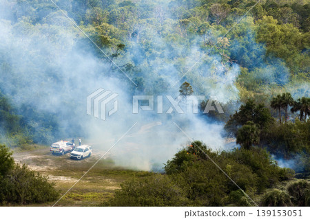 Wildfire sweeps through Florida dry forested area, with firefighters using hoses and tools to control crackling flames and smoke clouds spreading through the tree line Wildfire sweeps through Florida dry forested area, with firefighters using hoses and tools to control crackling flames and smoke clouds spreading through the tree line 139153051