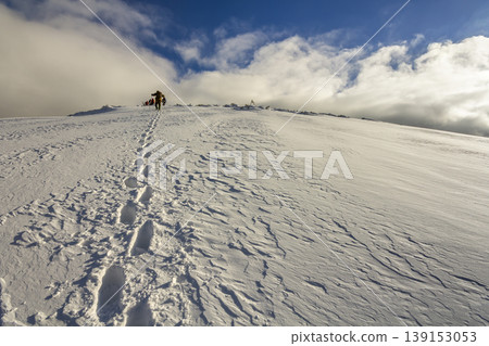 Wide view on the snowy hill with footprints and far away hiker walking up with backpack in the mountains 139153053