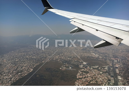 View through airplane window of commercial jet plane wing flying high in the sky ove big city. Air travelling concept 139153078