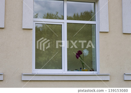 View from outside of big window with bouquet of bright paper flowers and reflection of green trees. 139153080