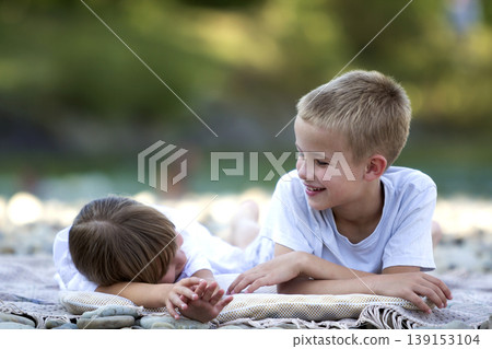 Two young happy cute blond laughing children, boy and girl, brother and sister having fun on pebbled beach on blurred bright sunny summer bokeh background. Friendship and perfect holiday concept. Two young happy cute blond laughing children, boy and girl, brother and sister having fun on pebbled beach on blurred bright sunny summer bokeh background. Friendship and perfect holiday concept. 139153104