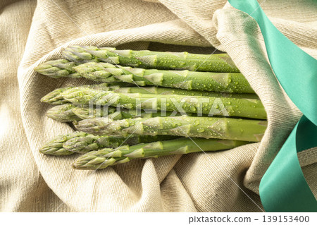 A photograph of spring vegetables, with fresh green asparagus arranged and glistening with water droplets. A photograph of spring vegetables, with fresh green asparagus arranged and glistening with water droplets. 139153400