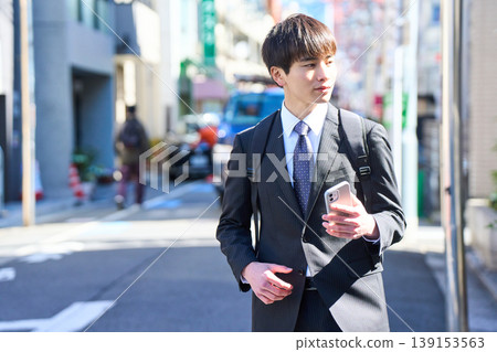 A young Japanese businessman answers the phone in the street while out on sales calls. A young Japanese businessman answers the phone in the street while out on sales calls. 139153563