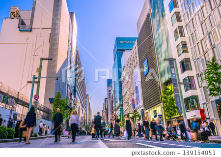 Tokyo cityscape, April 12th. Ginza pedestrian zone bustling with foreign tourists. A long line of foreigners resting on the curb. Tokyo cityscape, April 12th. Ginza pedestrian zone bustling with foreign tourists. A long line of foreigners resting on the curb. 139154051