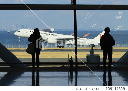 Passengers looking at the runway from the international area of Haneda Airport's Terminal 2 Silhouette of passengers looking at the runway Passengers looking at the runway from the international area of Haneda Airport's Terminal 2 Silhouette of passengers looking at the runway 139154839