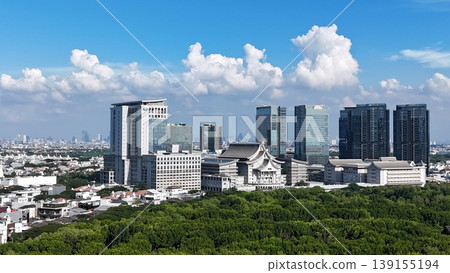 An aerial perspective captures a lush, dense mangrove forest split by a winding river, leading toward a distant urban skyline featuring white arched bridges under a vast, bright blue sky in Indonesia. 139155194